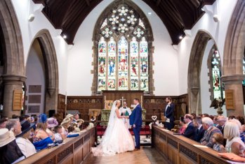 Bride and Groom standing in front of the altar receiving a blessing in front of their family and friends