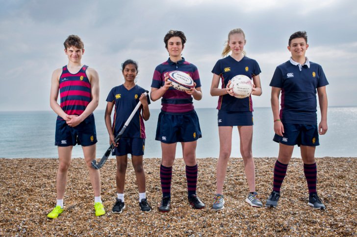  Pupils in games kit on the beach holding different sports equipment 