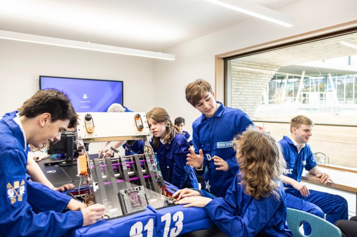  Robotics Team in the Richard Cairns Building working on a project together in their blue boiler suits 