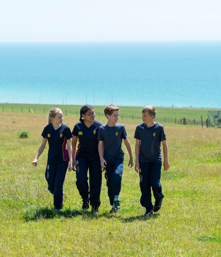  Pupils in their games kit walking through a field in the South Downs with the sea in the background 