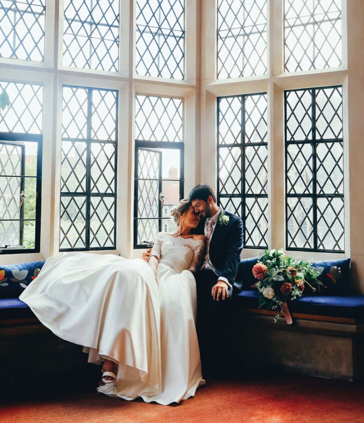  Bride and Groom sitting on a bench in the library in front of the windows 