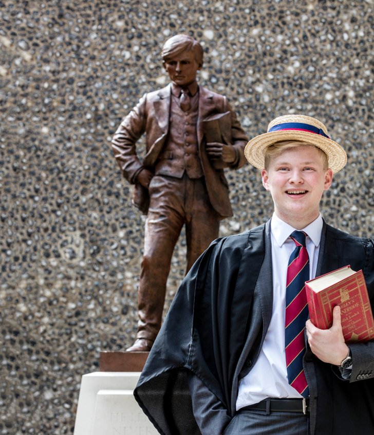  Prefect standing in front of the War Memorial outside the Chapel in their gown and boater 