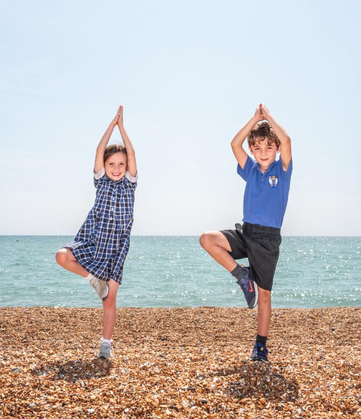  Pre-Prep pupils standing on one leg practicing yoga on the beach on a sunny day 