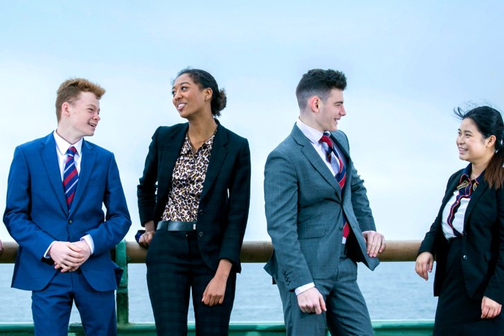  Sixth Form pupils in suits standing talking together on Brighton seafront 