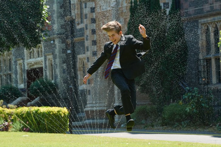  Pupil enjoying jumping through the sprinklers in school uniform on the grass in the Quad 