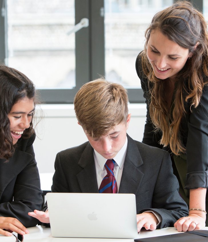  Pupils and their teacher gathered around a laptop looking at a questions on a laptop in a French lesson 