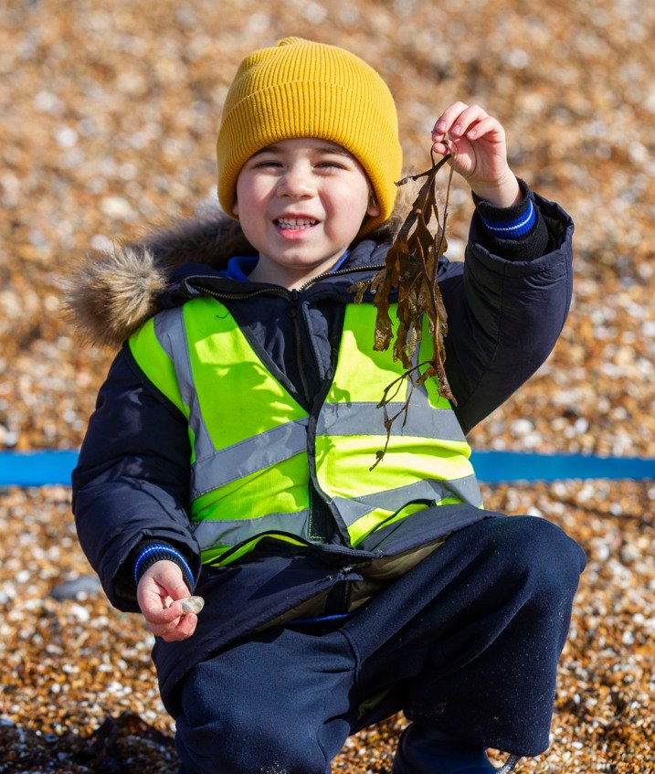  re-Prep pupil holding seaweed and sitting on the beach at Beach School 