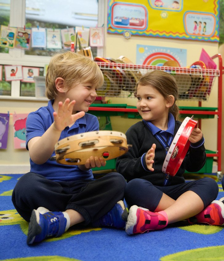  Nursey pupils sitting on the carpet playing the tambourine in a music lesson 