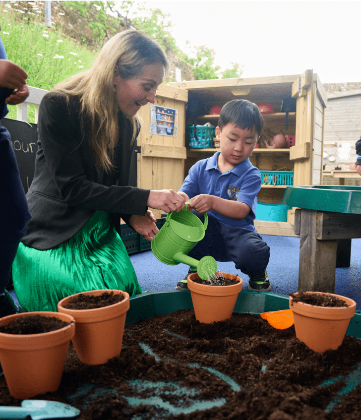  Teacher and Nursery pupil in the playground garden watering the plants with a watering can 