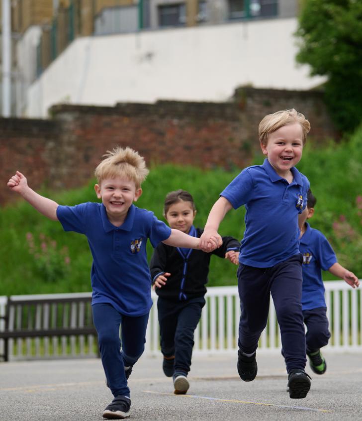  Nursery pupils holding hands and running through the playground together 