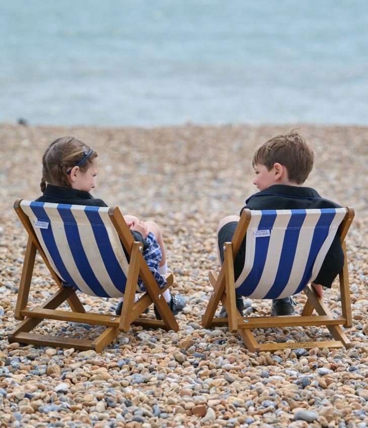  Pre-Prep pupils sitting in deck chairs on the beach chatting and looking at the sea 