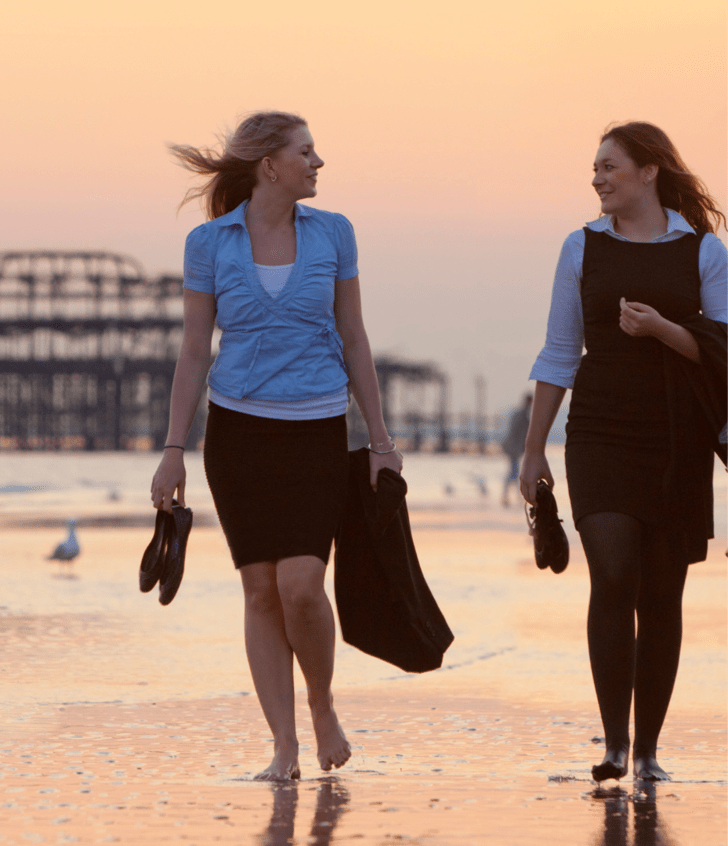  Sixth Form pupils in suits holding their jackets and shoes and walking along the sand on the beach in front of the Brighton Pier 