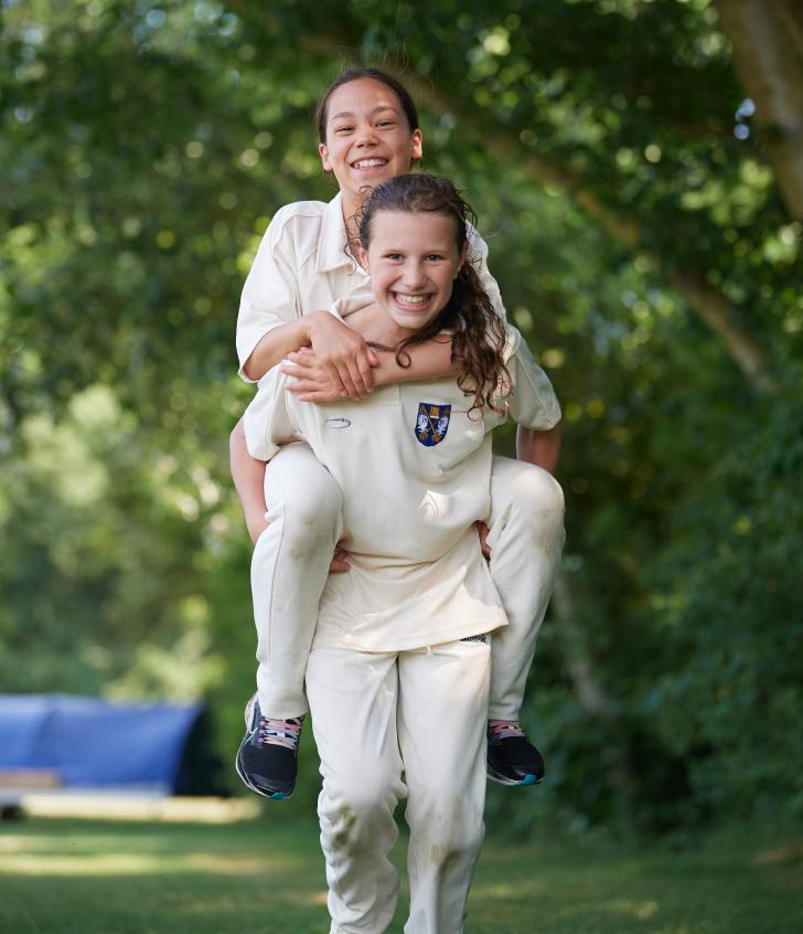  Prep School pupils giving each other a piggyback in cricket whites at a Cricket match 