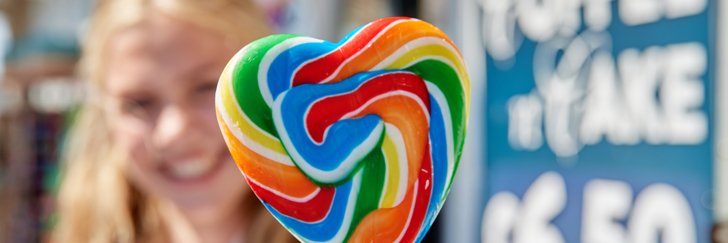  Pupil smiling whilst holding a rainbow lollipop shaped like a heart 