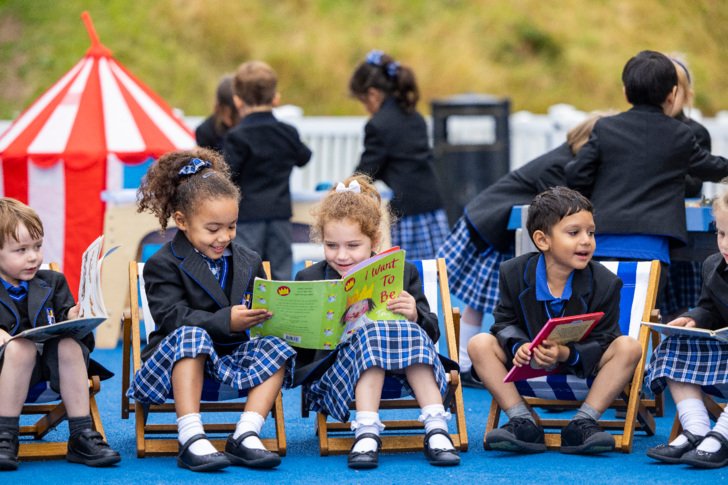  Pre-Prep pupils sitting in the playground and reading a book together at break time 