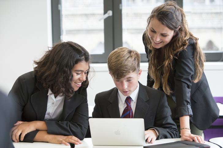  Pupils and their teacher gathered around a laptop looking at a questions on a laptop in a French lesson 