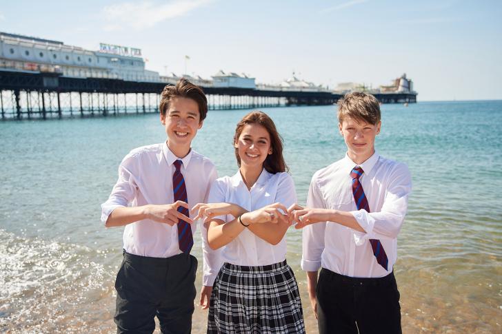  Pupils standing in front of the Pier in the sea with their hands forming hearts 