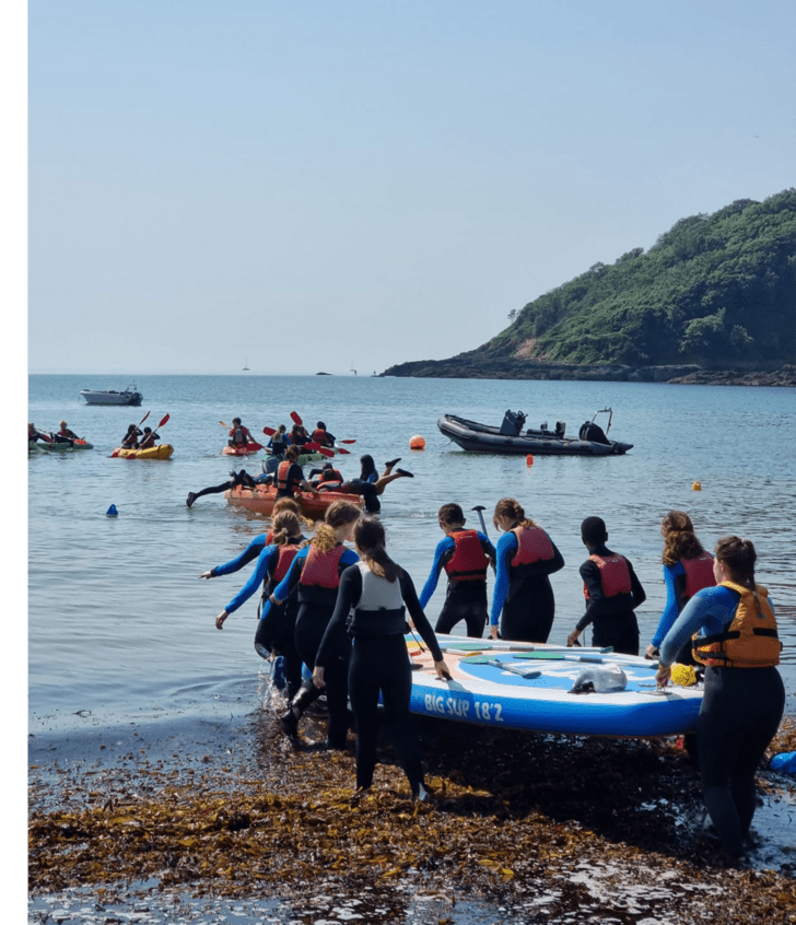  Prep School pupils carrying a large paddleboard into the sea on a school residential trip to Cornwall 