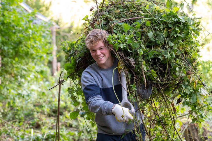  Pupil on Make A Difference Day holding weeds above his head on a shovel in a garden 