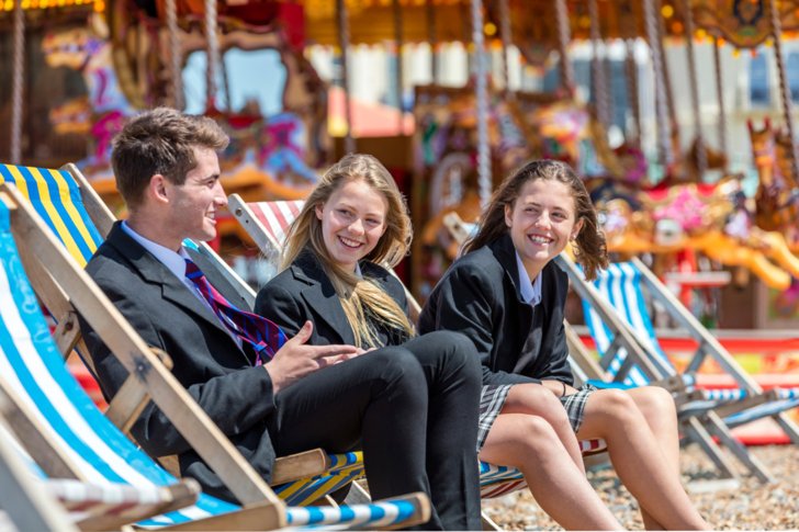  Pupils in their uniform sitting on Brighton Beach in deck chairs 