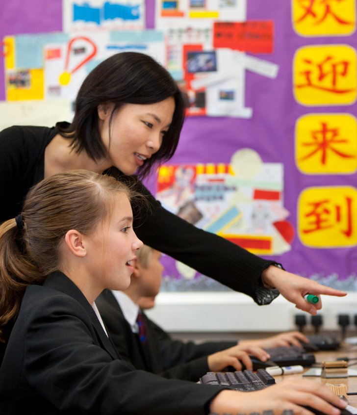  Mandarin teacher showing a Lower School pupil something on a computer in a Mandarin lesson 