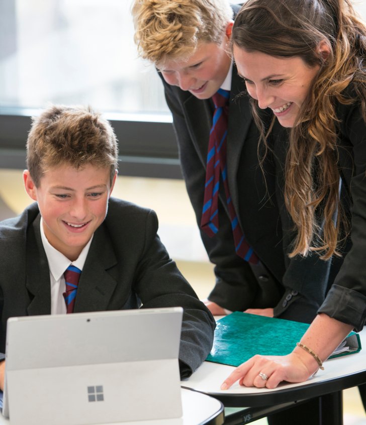  Pupils and their teacher gathered around a laptop looking at a questions on a laptop in a French lesson 