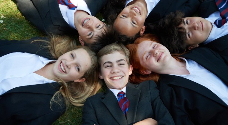  Pupils lying on the grass in a circle in their uniform smiling 