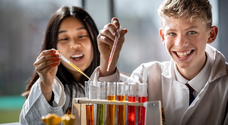  Pupils putting different coloured substances into test tubes with pipettes as part of a science experiment 