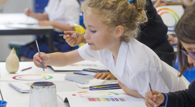  Prep School pupil dipping their paintbrush into water and painting the colour wheel in an Art lesson 