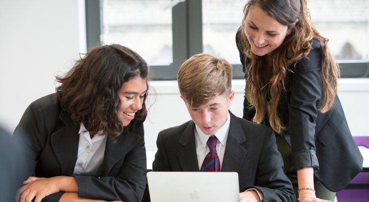  Pupils and their teacher looking at something on a laptop in a lesson 