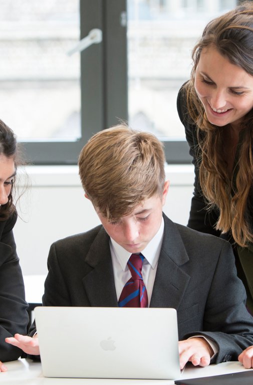  Pupils and their teacher gathered around a laptop looking at a questions on a laptop in a French lesson 