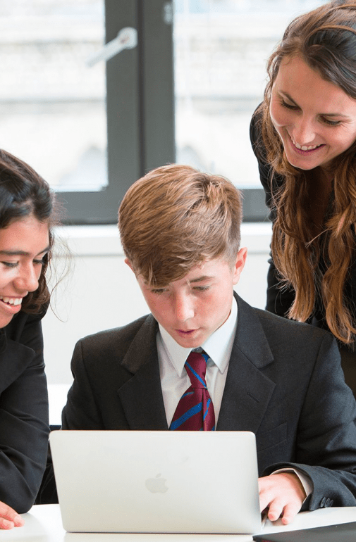  Pupils and their teacher gathered around a laptop looking at a questions on a laptop in a French lesson 